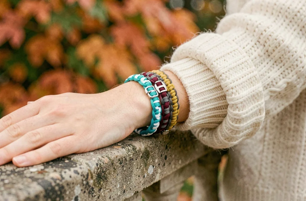 Femme portant des bracelets en paracord empilés aux couleurs turquoise-blanc, bordeaux-gris et jaune moutarde-charbon sur son poignet