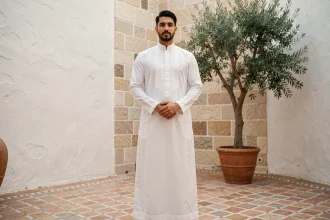 Homme arabe portant une thobe blanche taillée avec col mandarin dans une cour marocaine contemporaine, mise en valeur de la silhouette masculine